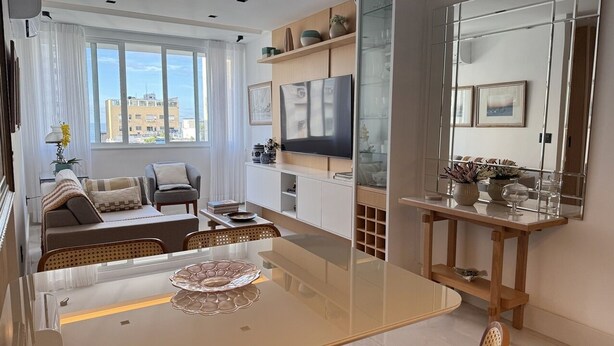 A modern living room with a glass dining table, a sofa, a TV, and a large mirror. - Ipanema with SEA VIEW and total comfort (Rio de Janeiro)
