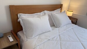 A neatly made bed with white bedding and pillows, a wooden headboard, a bedside table with a lamp, and a remote control on the table. - Ipanema with SEA VIEW and total comfort (Rio de Janeiro)
