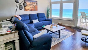 Ein Wohnzimmer mit einem blauen Sofa, einem Couchtisch und Blick auf den Ozean durch große Fenster.