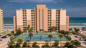 Ein mehrstöckiges Hotel mit Tennisplatz, Palmen und Blick auf den Ozean.
