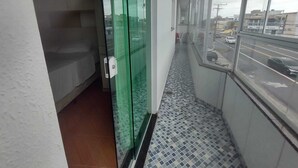 Un couloir étroit au sol carrelé, une porte en verre et une vue sur la rue par une grande fenêtre.