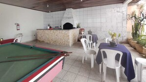 Une table de billard, un espace barbecue agrémenté d’un mur en pierre, et un coin salon extérieur avec des chaises et des tables.