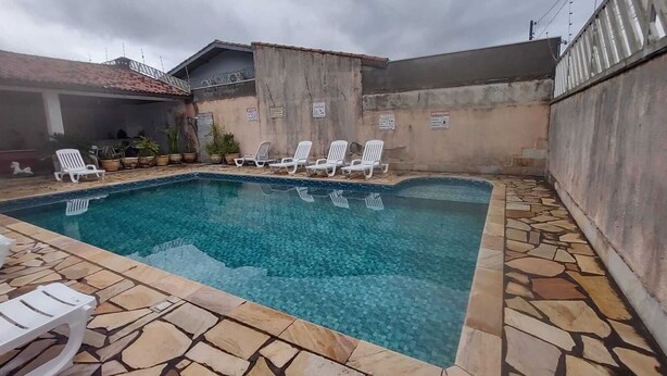 Une piscine rectangulaire à l’eau d’un bleu limpide, entourée de carreaux de pierre. Des chaises longues blanches sont alignées le long du bord de la piscine.