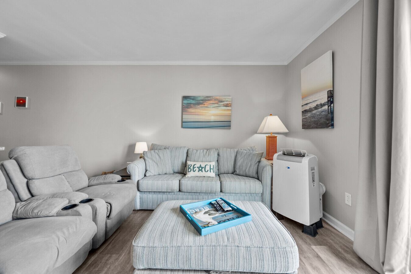 A living room with a grey sectional sofa, a small ottoman, a lamp, and a TV stand.