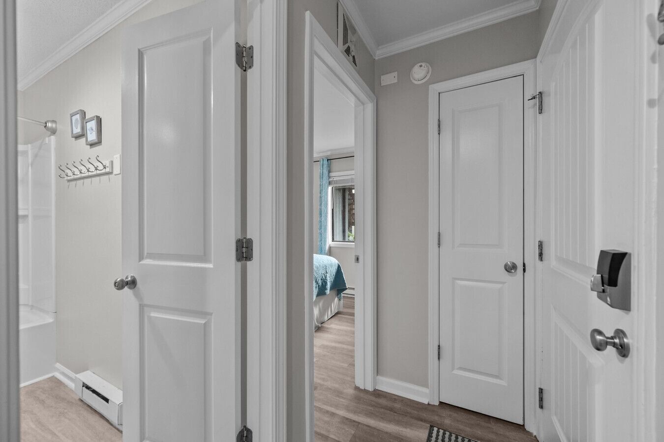 A hallway with white doors, a coat rack, and a blue towel on a bed in the background.