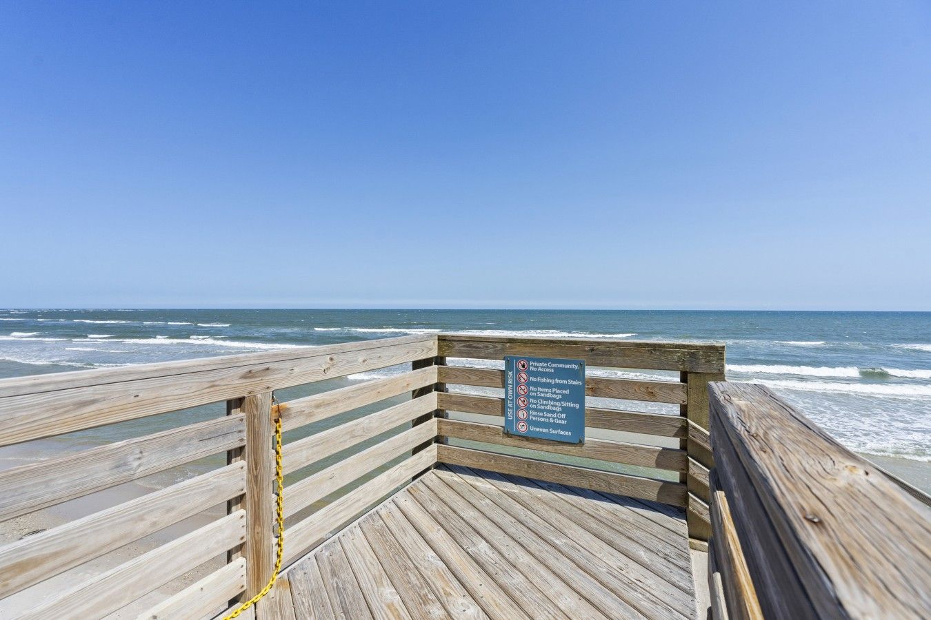 A wooden boardwalk leading to the ocean with a sign indicating it is a private community with no access.