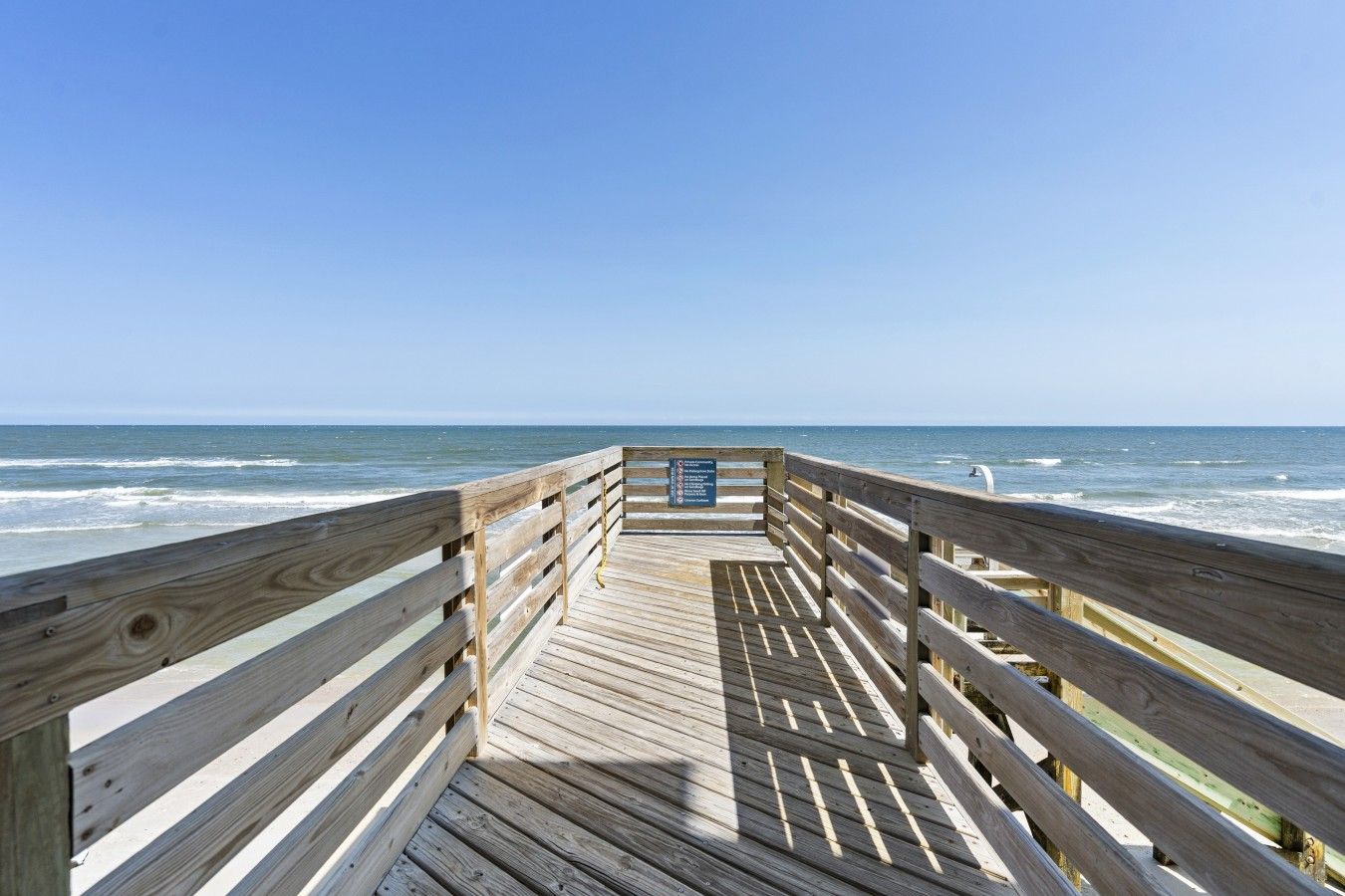 A wooden pier leading to the ocean with a signboard in the center.