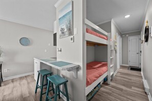 Une chambre d’enfant avec des lits superposés, un bureau et deux tabourets.