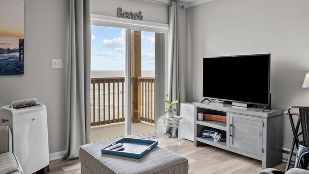 Una sala de estar moderna con un televisor grande, una cafetera y un balcón con vista a la playa.