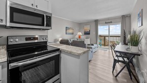 Una cocina moderna con horno empotrado y microondas, un comedor con mesa y sillas, un sofá y un balcón con vistas.