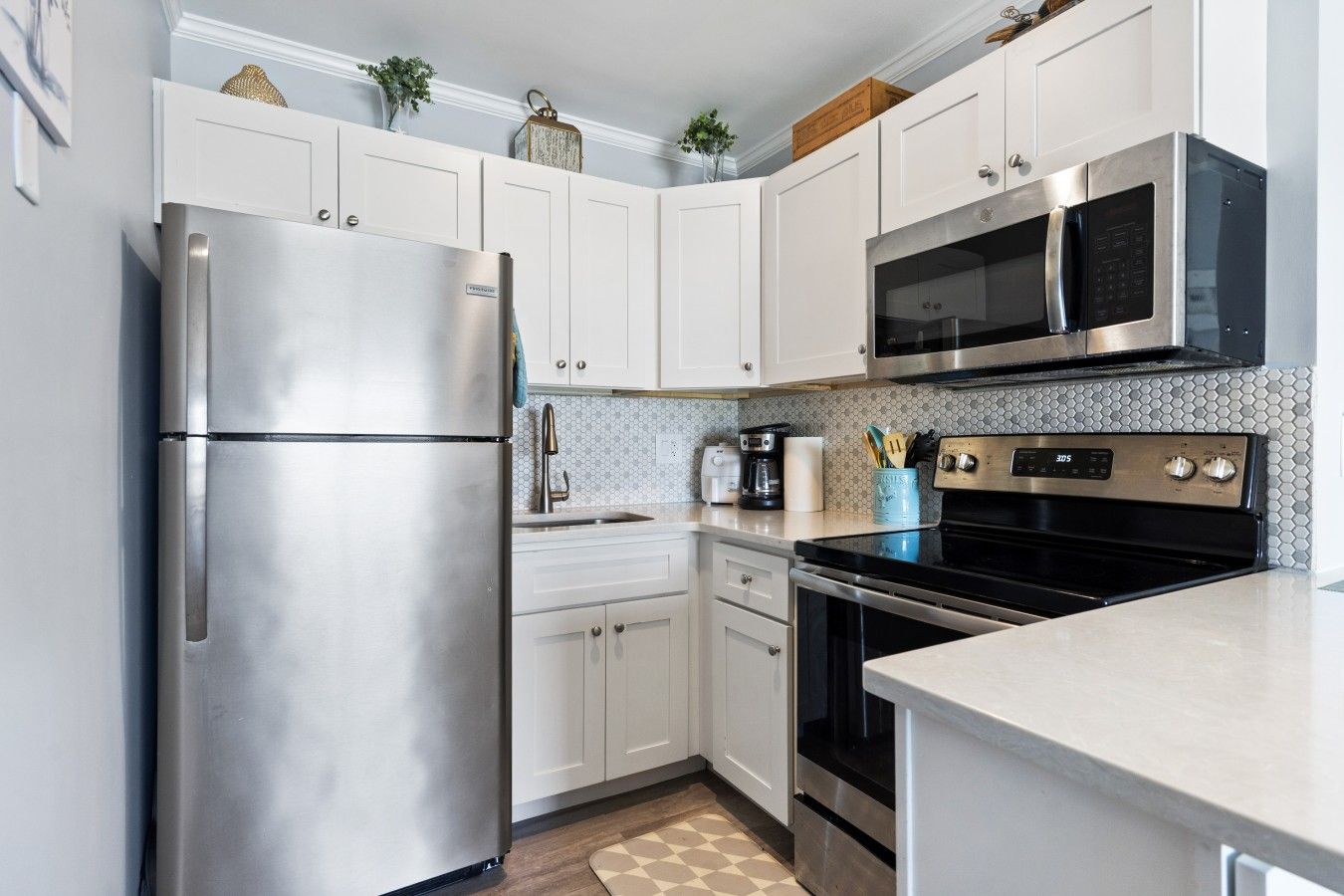 A modern kitchen with stainless steel appliances, white cabinetry, and a tiled backsplash.