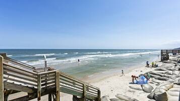 A beach with a wooden staircase leading down to the shore, a sandy beach with rocks, and the ocean in the background.