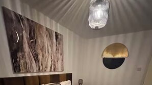 Ein modernes Schlafzimmer mit einem großen Bett, einer Marmor-Wandkunst, einer außergewöhnlichen Deckenleuchte und einer runden Wandlampe.