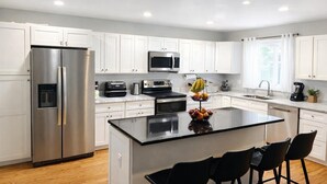 Una cocina moderna con armarios blancos, electrodomésticos de acero inoxidable, una isla central con sillas y un frutero.