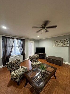 A living room with a ceiling fan, a TV, a sofa, two patterned armchairs, and a coffee table with a plant. - A lovely Condo in the sky (Atlanta)