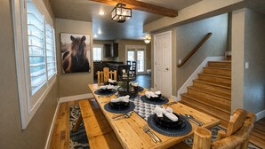 A dining area with a long wooden table set for four, a staircase to the right, and a kitchen in the background. - Park City Adventure Retreat Walk to Dining and Skiing 470 (Park City)