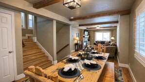 A dining area with a long wooden table set for four, a staircase, and a cozy living room in the background. - Park City Adventure Retreat Walk to Dining and Skiing 470 (Park City)