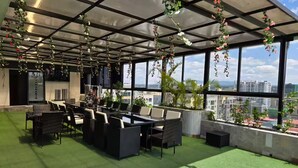 Eine Dachterrasse mit Außenbereich, großen Fenstern und hängenden Pflanzen.