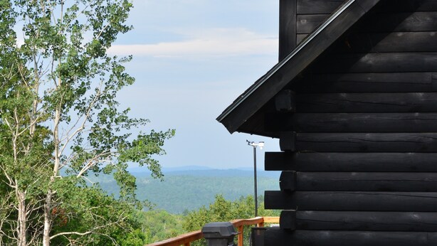 A wooden deck with a railing, a propane grill, and a view of a mountainous landscape.