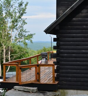 A wooden deck with a railing, a propane grill, and a view of a mountainous landscape.