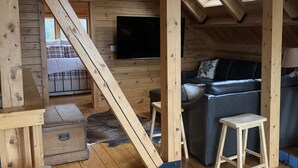 A cabin interior with a wooden floor, a sofa, a television, and a ceiling fan.