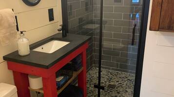 A bathroom with a glass-enclosed shower, a white toilet, a red vanity with a black countertop, and a mirror above the sink.