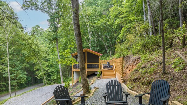 A cabin with a deck, surrounded by trees, and featuring a fire pit with chairs. - Private & Modern Creekside Cabin w/ Hot Tub and Fire Pit - Great Location! (Cherry Log)