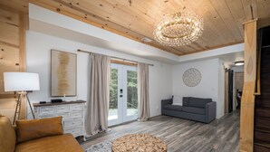 A spacious living room with a wooden ceiling, a round wooden coffee table, a grey sofa, and a large window with curtains. - Private & Modern Creekside Cabin w/ Hot Tub and Fire Pit - Great Location! (Cherry Log)