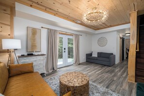 Un salón amplio con techo de madera, una mesa redonda de madera, un sofá gris y un ventanal con cortinas.
