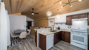 A modern kitchen with wooden cabinets, a built-in dishwasher, and a large stove. - Private & Modern Creekside Cabin w/ Hot Tub and Fire Pit - Great Location! (Cherry Log)
