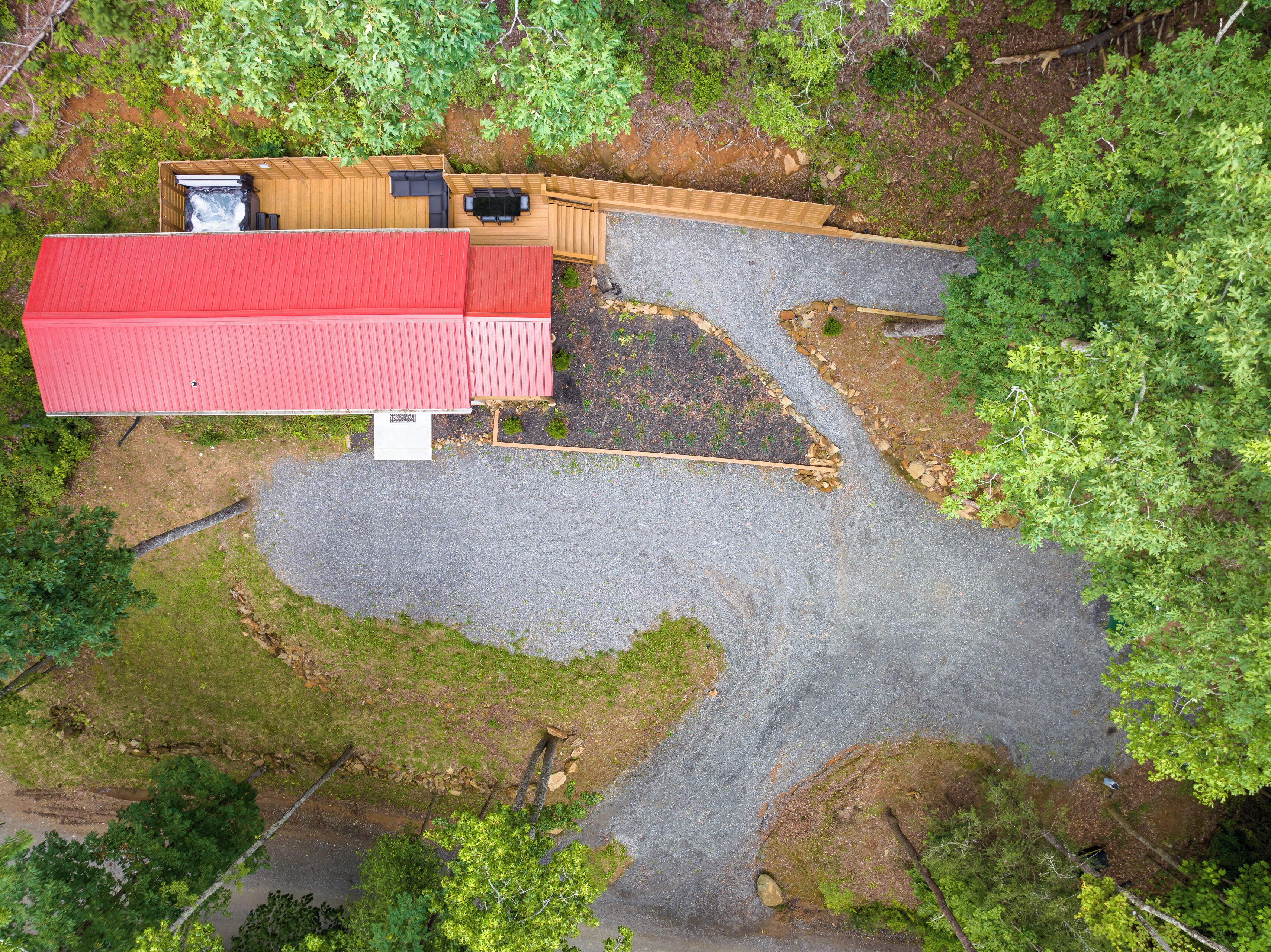 An aerial view of a property with a red-roofed building, a wooden deck, and a gravel driveway.