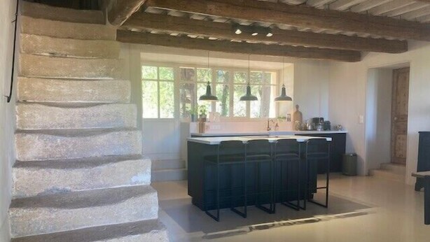 Una cocina con una isla central, una escalera de piedra e iluminación colgante.