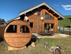 A wooden cabin with a large circular window, a dining area, and a satellite dish. - Chalet de la Louve in La Pesse Dogs welcome in fenced garden (LA PESSE)