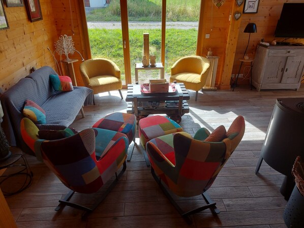 Un acogedor interior de cabaña con un sofá, dos sillones coloridos, una mesita de centro y una televisión.