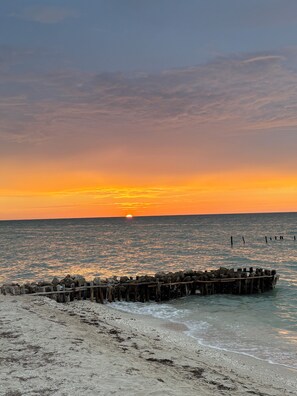 A beach with a wooden pier extending into the water, a clear sky, and the sun setting on the horizon. - Enjoy the beach and the sunset in this beautiful beachfront home (Chuburná)