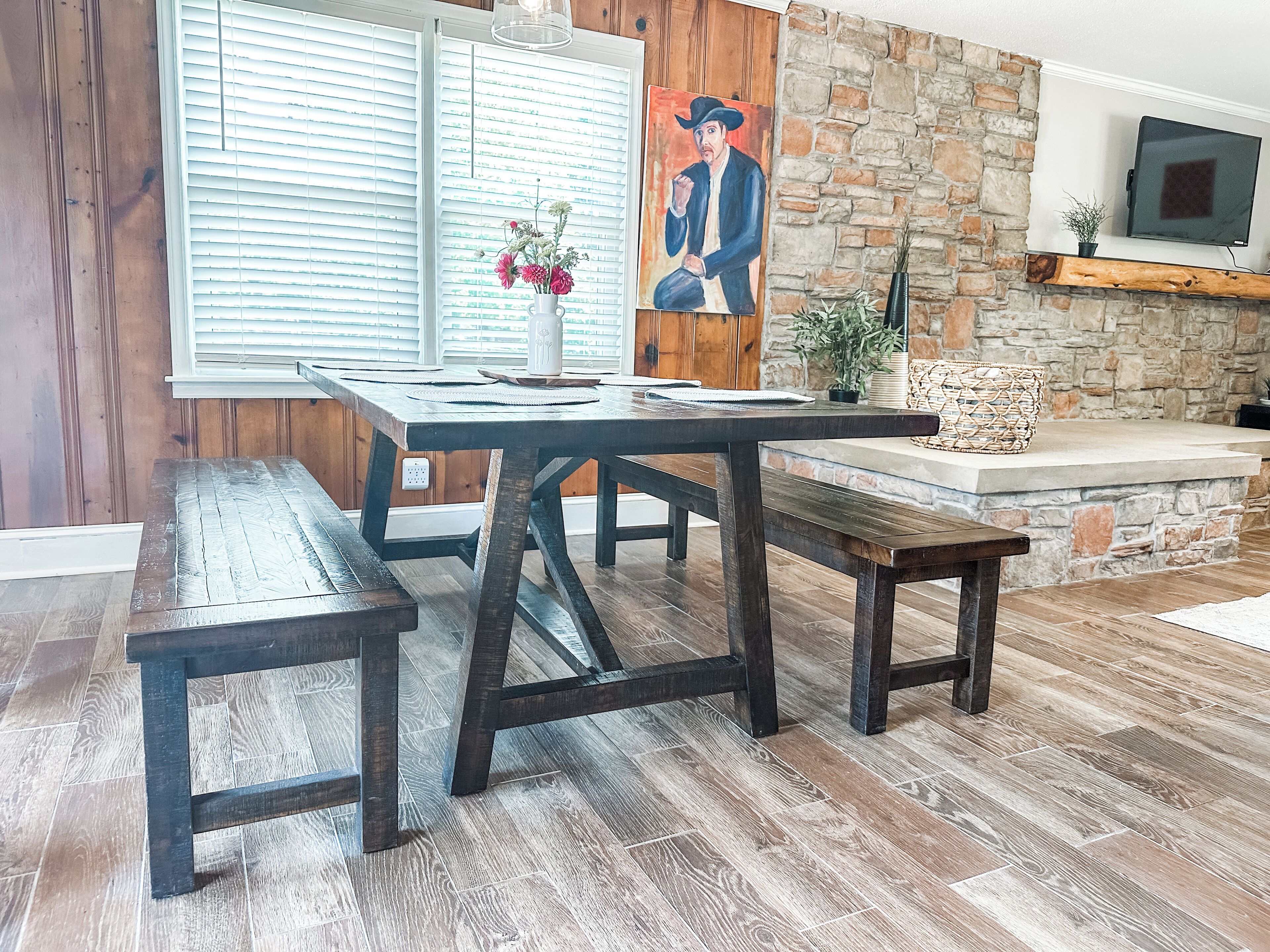 Un coin repas avec une table et des bancs en bois, un mur en pierre et un tableau accroché au mur.