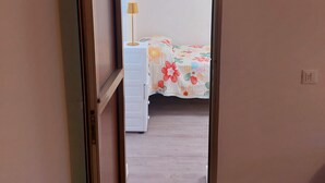 Ein Flur, der zu einem Schlafzimmer mit Bett, Nachttisch und Lampe führt.
