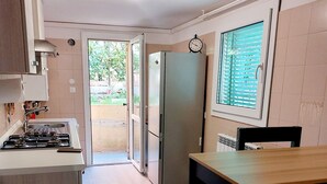 Eine kleine Küche mit einem Gasherd, einem Kühlschrank und einem Fenster mit Jalousien.