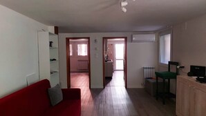 Ein Wohnzimmer mit einem roten Sofa, einem Holzschrank und einem Fernseher. Es gibt eine Küchenzeile mit einem Heizkörper und einem Fenster.