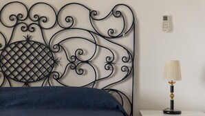 Un lit avec une couverture bleue, une tête de lit décorative en métal, une lampe de chevet et un thermostat fixé au mur.