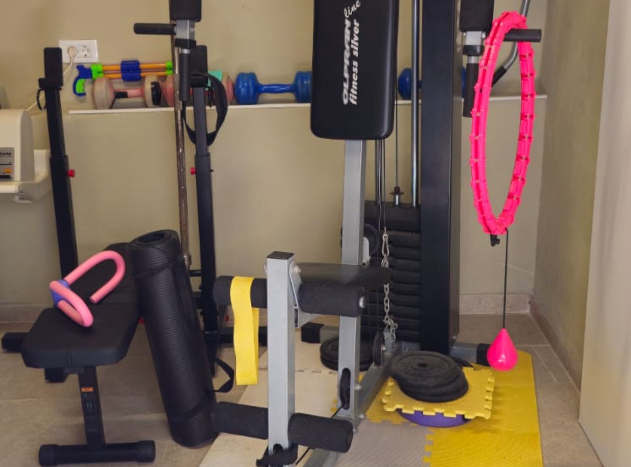 Un gimnasio con equipo de ejercicio, incluyendo una banca, mancuernas, una estructura para sentadillas y bandas de resistencia.