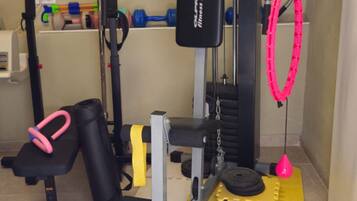 Un gimnasio con equipo de ejercicio, incluyendo una banca, mancuernas, una estructura para sentadillas y bandas de resistencia.