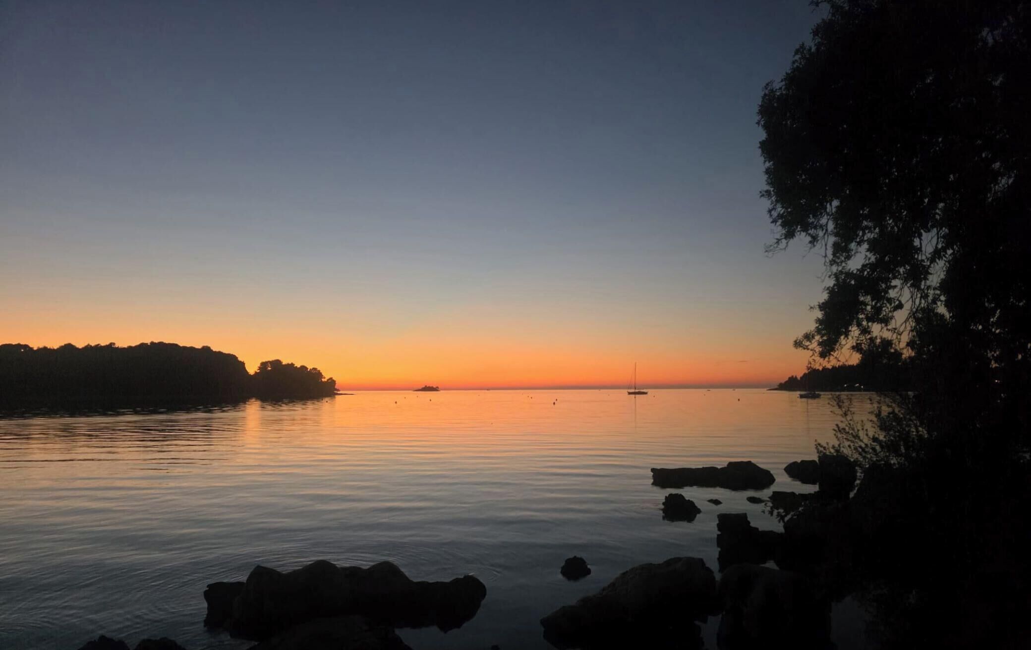 Un lac paisible au coucher du soleil, avec des bateaux et une rive bordée d’arbres.