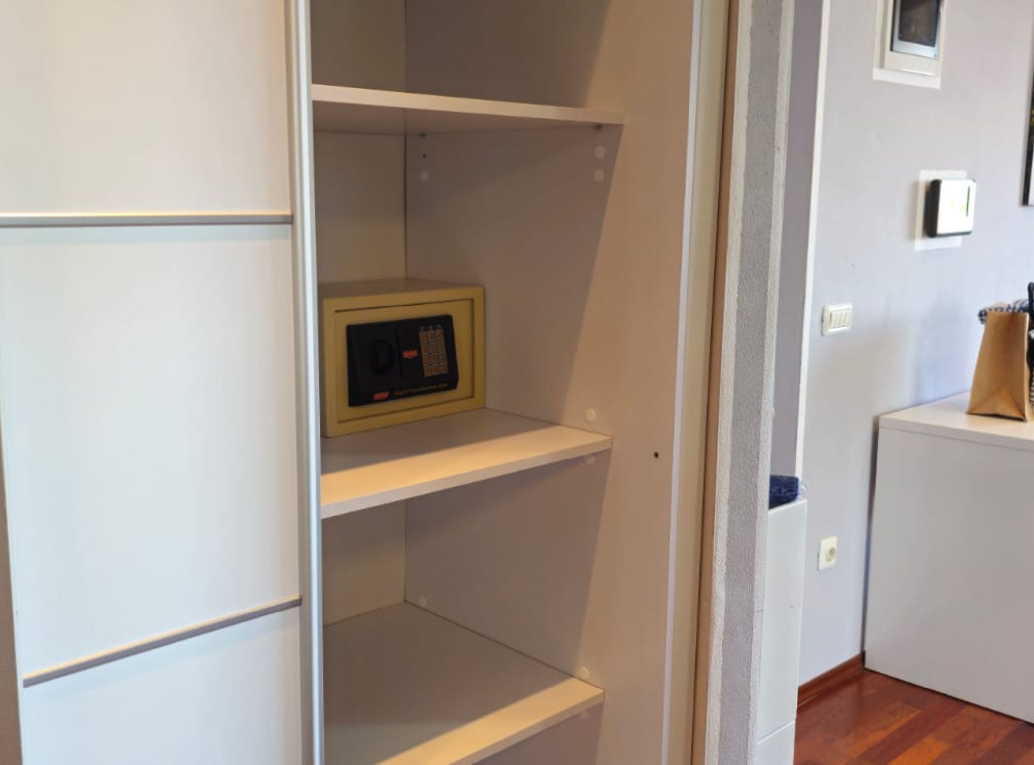 A room with white walls, a wooden floor, and a white cabinet with a small electronic device on the top shelf.