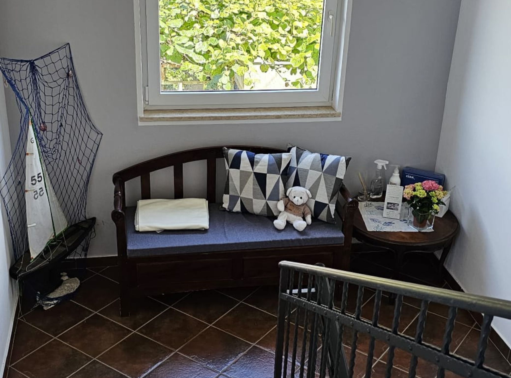 A small, cozy room with a wooden bench, a sailboat model, and a window with a view of greenery.