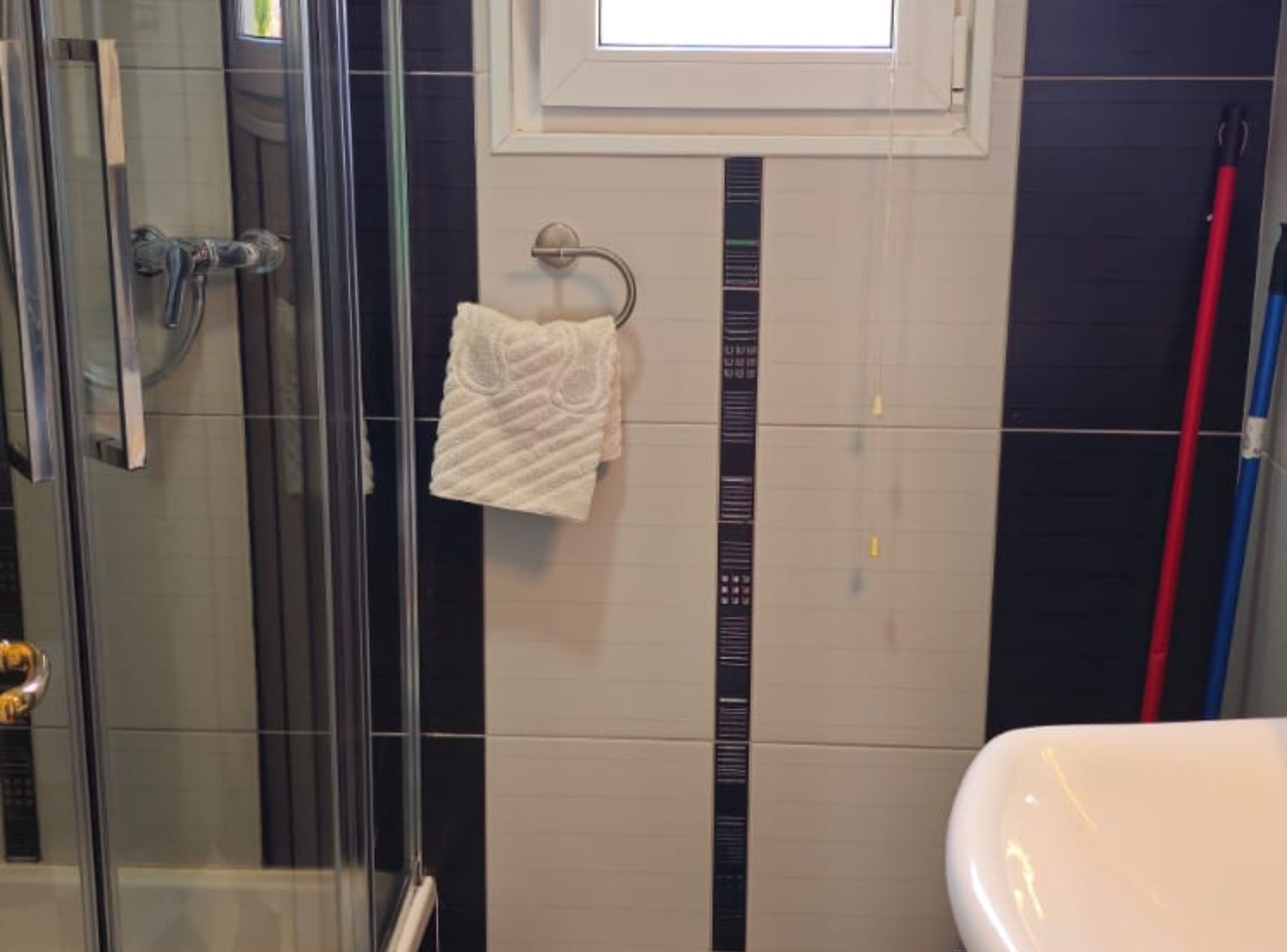 A bathroom with a glass shower enclosure, a white sink, and a towel hanging on a rack.