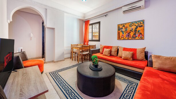 A living room with a sofa, coffee table, and TV. There is a dining area with chairs and a table.