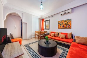 Una sala de estar con sofá, mesa de centro y televisor. Hay un comedor con sillas y una mesa.