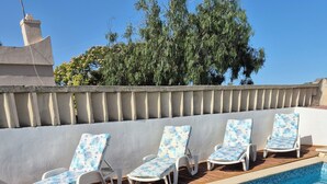 En swimmingpool med blå mosaikplattor på botten, omgiven av vita solstolar med blått blommönster.