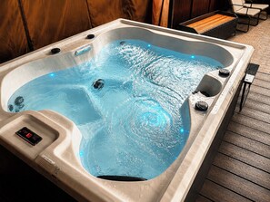 A hot tub with a digital control panel, a wooden deck, and a seating area with chairs. - The Cloud House Spa Retreat Hoole (Chester)